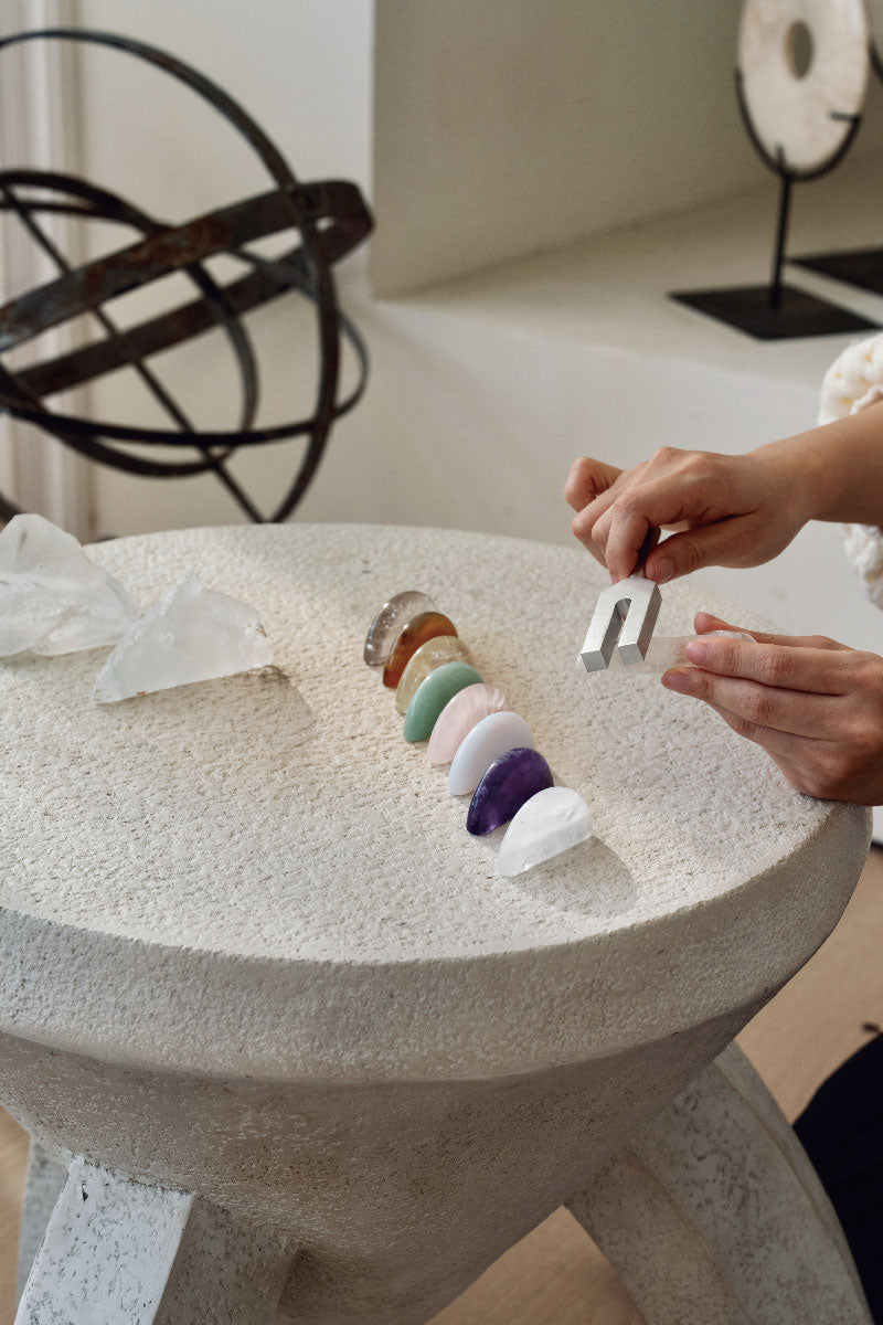 Hand using a tuning fork over a row of chakra stones for final attunement to stabilize crystal vibrations.