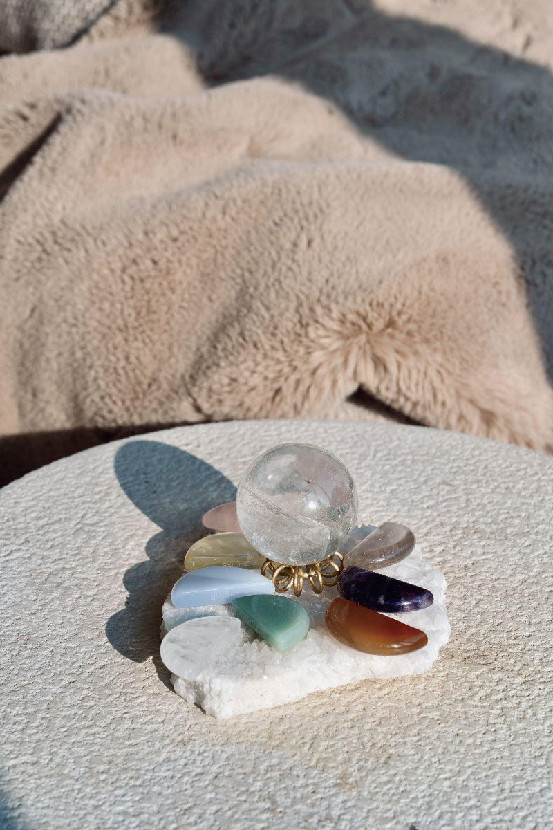 High-vibration Himalayan Quartz base activating a clear sphere and colorful chakra stones through proximity resonance under sunlight
